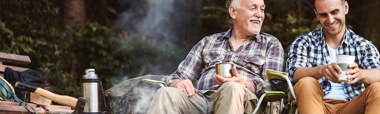 Two men sitting by a fire in the woods.